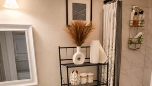 A bathroom with a white sink, a toilet, a bathtub, a shelf with toiletries, and a framed picture on the wall. - Modern2Bed2Bath Oasis 3 mins to LSUlFreeParking (Baton Rouge)