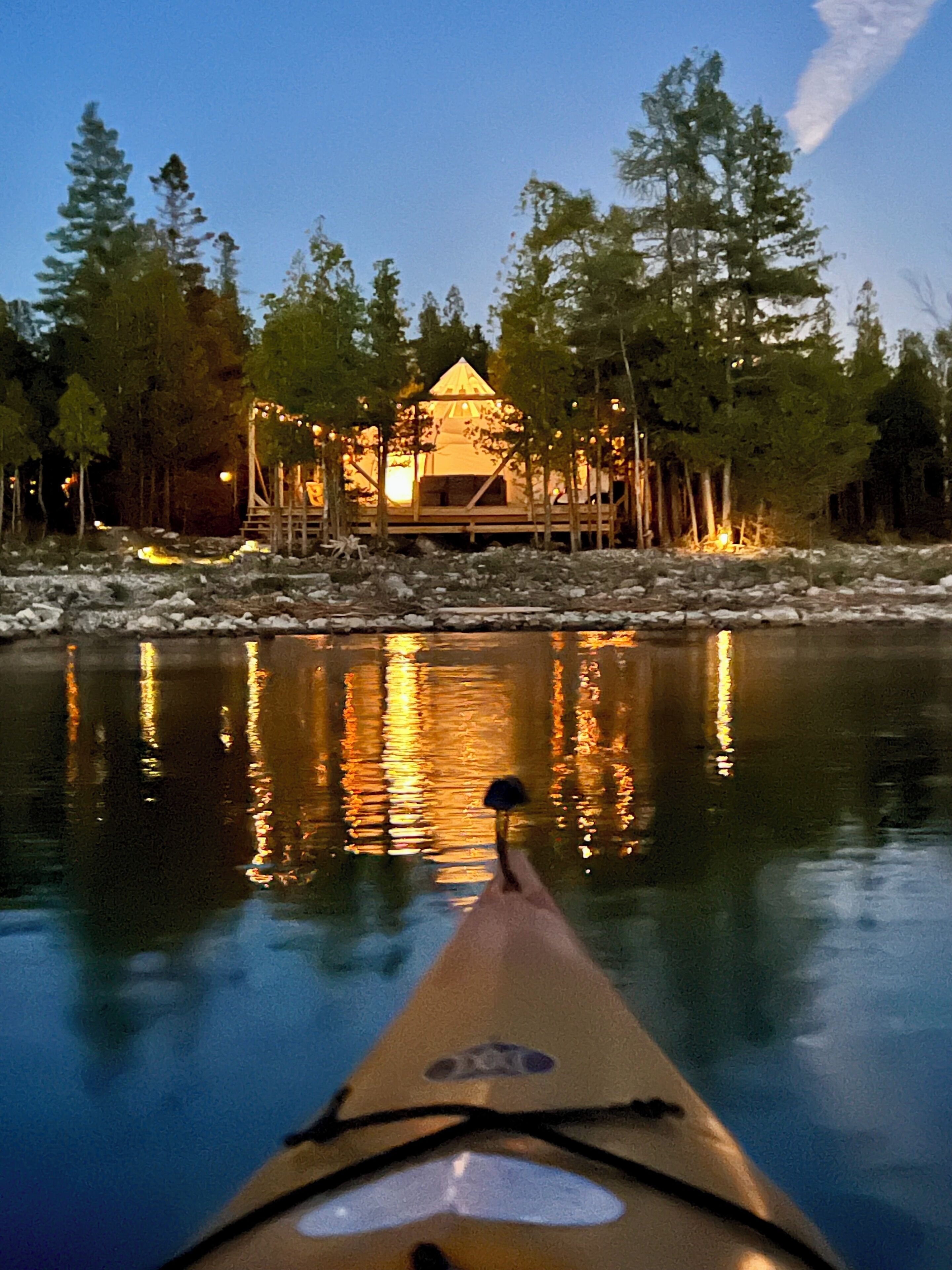 Un kayak su un fiume tranquillo con un molo di legno e una piccola casetta sullo sfondo.