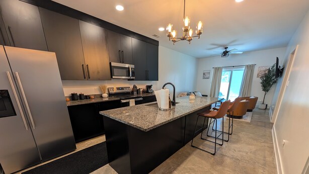 A modern kitchen with a central island, dark cabinetry, stainless steel appliances, and a ceiling fan. - Dune Haus + Indiana National Dunes Park (Portage)