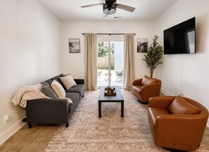 Ein Wohnzimmer mit einer Couch, zwei Sesseln, einem Couchtisch und einem an der Wand befestigten Fernseher.