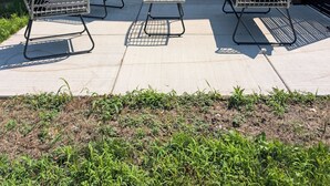 A patio with two metal-framed chairs and a small table, a sliding glass door, and a large air conditioning unit. - Dune Haus + Indiana National Dunes Park (Portage)