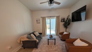 A living room with a sofa, armchairs, a coffee table, a ceiling fan, and a large window with curtains. - Dune Haus + Indiana National Dunes Park (Portage)