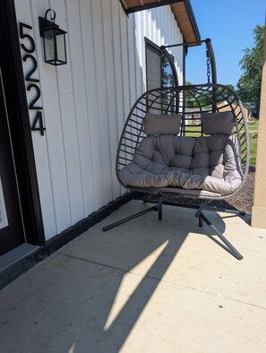 A hanging chair with cushions, a black metal railing, and a white building with the number 5224. - Dune Haus + Indiana National Dunes Park (Portage)