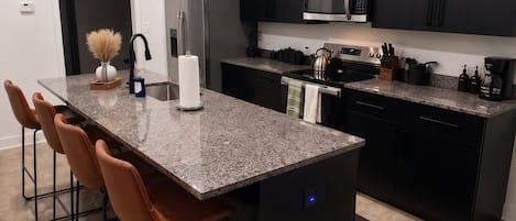 Una cocina moderna con una isla central, armarios negros, electrodomésticos de acero inoxidable y un candelabro.