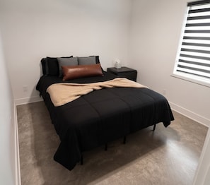 Ein Schlafzimmer mit einem Bett, Kissen, einem Nachttisch, einer Taschentuchbox und einem Fenster mit Jalousien.