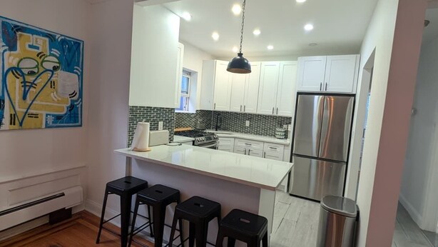 A modern kitchen with a central island, bar stools, and a stainless steel refrigerator.