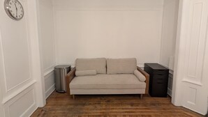 A room with a wooden floor, a beige sofa, a trash bin, and a black filing cabinet.