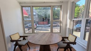 A room with a round wooden table, two chairs, large windows, and a ceiling light fixture.