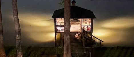 Un belvédère au bord d’un lac, illuminé la nuit, avec un sentier qui y mène.