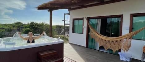 A hot tub on a wooden deck with a hammock and a building in the background.