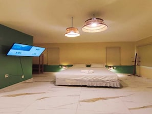 Una habitación de hotel con cama, dos lámparas colgantes, televisor en la pared y una mesita de noche.