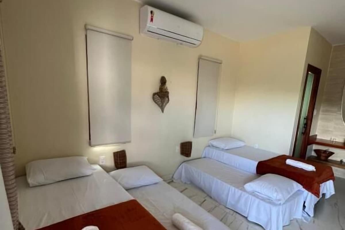 A hotel room with three beds, a wall-mounted air conditioner, and a small decorative item on the wall.