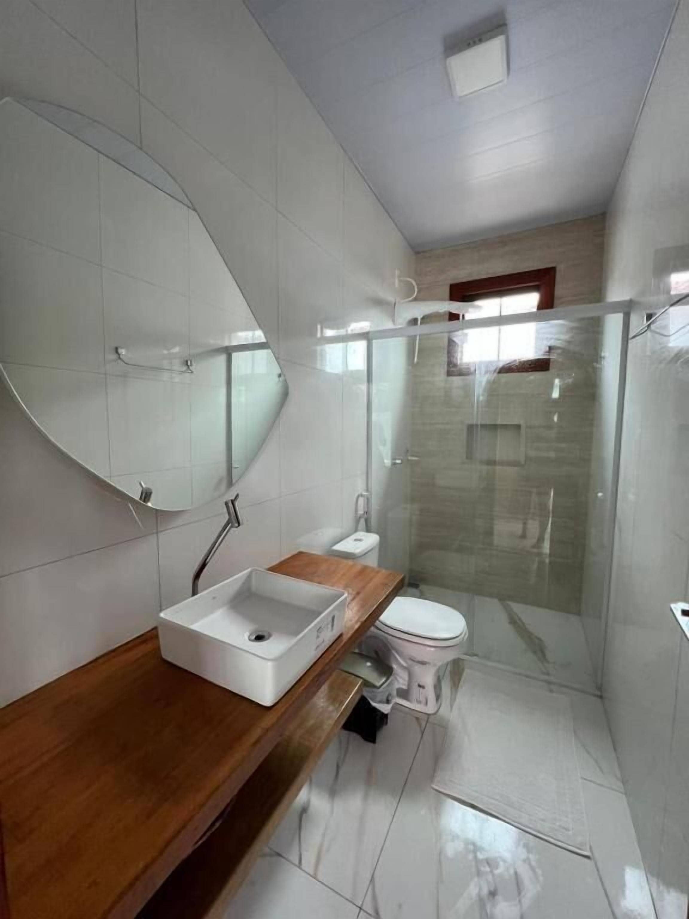 A bathroom with a wooden vanity, a white sink, a toilet, and a glass shower enclosure.