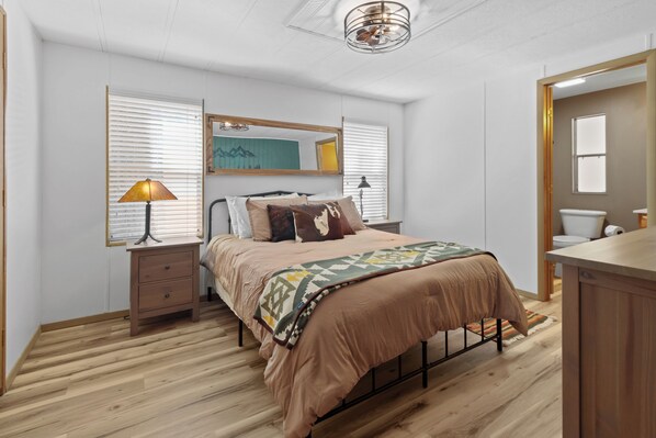 Une chambre à coucher avec un lit, des tables de chevet, un miroir et une fenêtre avec des stores.