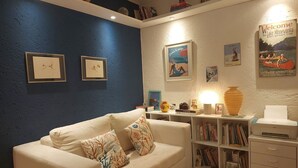 En stue med blå vægge, en hvid sofa med mønstrede puder, en reol og et indrammet velkommen-skilt.