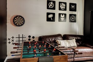 Ein Fußballtisch, eine Dartscheibe und verschiedene Wanddekorationen, darunter Superhelden-Symbole.