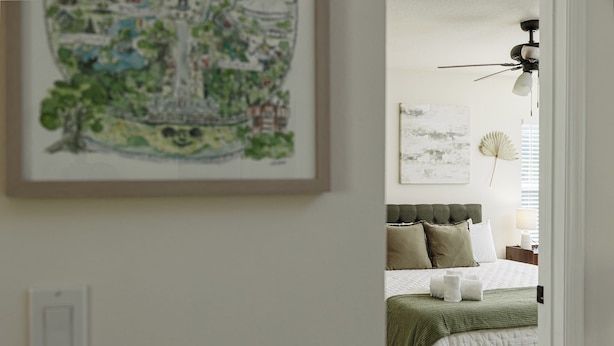 Ein Schlafzimmer mit einem Bett, Kissen, einem Deckenventilator und Kunstwerken an den Wänden.