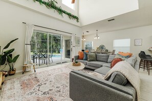 Ein geräumiger Wohnbereich mit einer großen Couch, einem Couchtisch und einem gemusterten Teppich. Eine Schiebetür führt auf eine Außenpatio mit einem Esstisch und Stühlen.