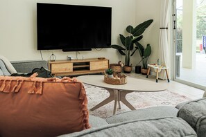 Ein Wohnzimmer mit Flachbildfernseher, grauen Sofas, einem Couchtisch und Topfpflanzen.