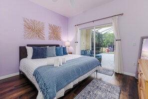 Un dormitorio con cama, mesita de noche, lámpara, ventana con cortinas y vistas al exterior.