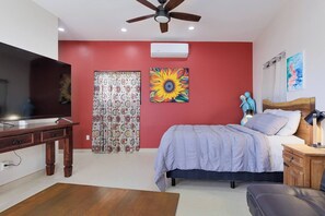 A bedroom with a bed, a TV, a ceiling fan, and a window with curtains. - Los Barriles Area Girasol Beach View (Spa Buenavista)
