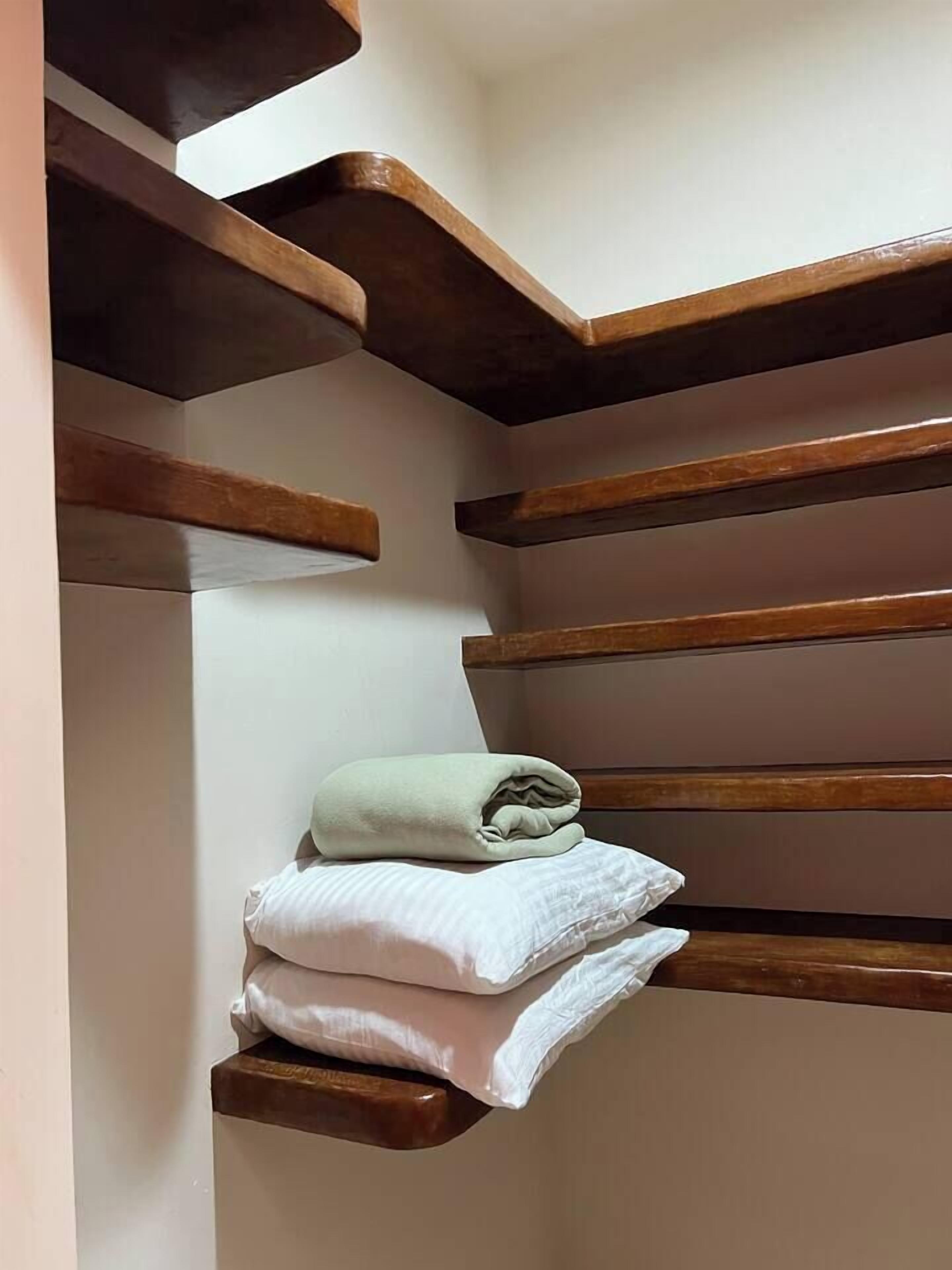 A corner of a room with a wooden staircase and a small shelf with folded towels.