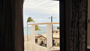 Une chambre avec vue sur la plage, un balcon agrémenté d’un palmier et un rideau à motifs.