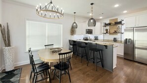 Een moderne keuken met een centraal eiland, barkrukken, hanglampen en roestvrijstalen apparatuur.