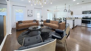 Een moderne woonkamer met een modulaire bank, een salontafel en een eethoek met een kroonluchter.
