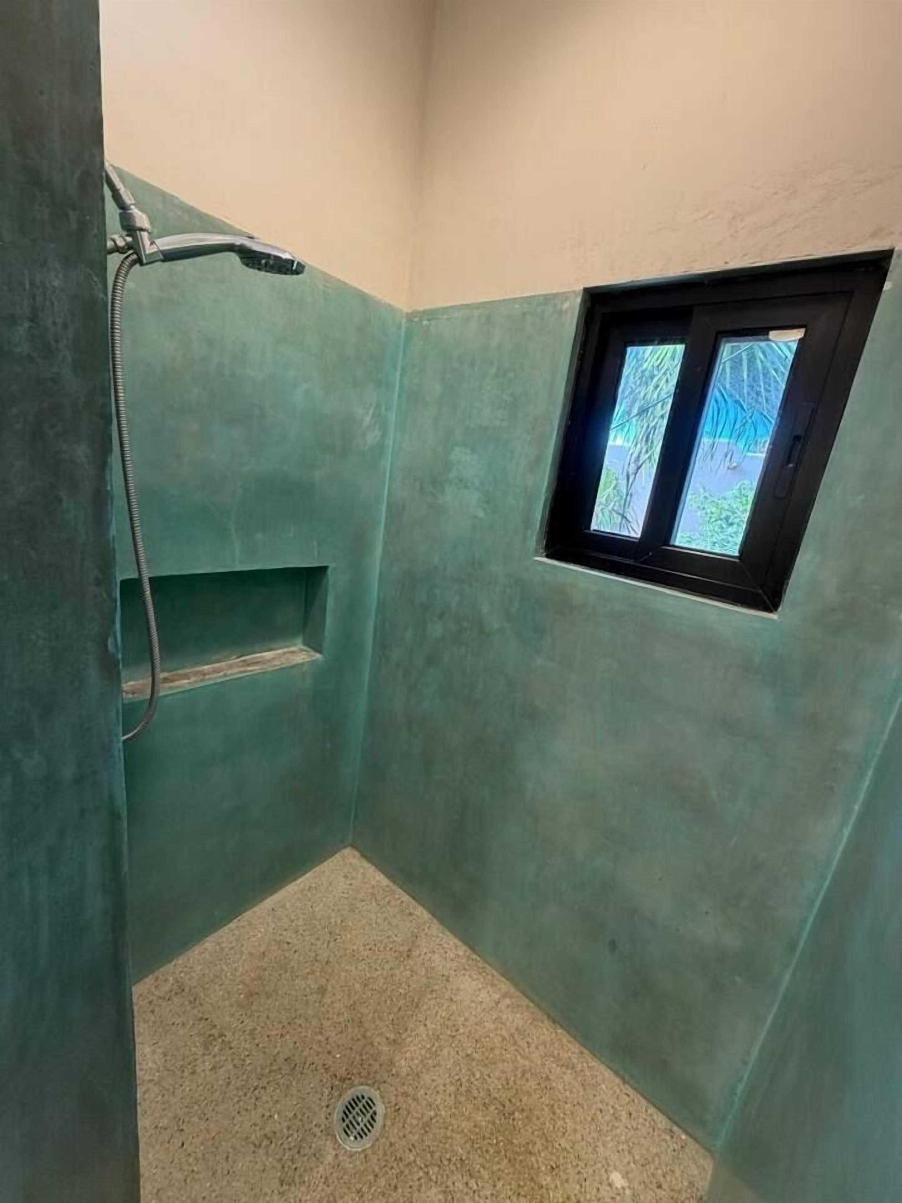 Un espacio de ducha pequeño y cerrado, con ventana, cabezal de ducha y desagüe.