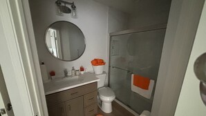 Un baño con inodoro, lavamanos, espejo, ducha y una alfombra.