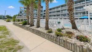 Un hotel con zona de piscina, palmeras y una cerca blanca.