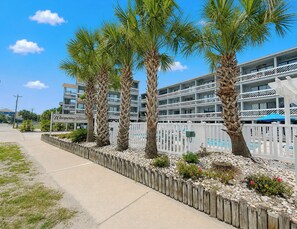 A hotel with a pool area, palm trees, and a white fence. - Whispering Sands II 204 - Second Row Complex (Oceanview unit) in Garden City Beach (Garden City Beach)