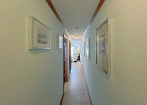 A hallway with framed pictures on the walls, a door on the left, and a window at the end. - Whispering Sands II 204 - Second Row Complex (Oceanview unit) in Garden City Beach (Garden City Beach)