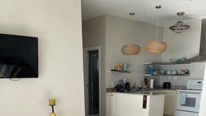 En moderne stue med en grå sofa, et lille sofabord med stearinlys, og et køkkenområde med komfur, ovn og hængende pendellamper.