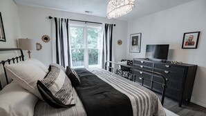 A bedroom with a bed, a TV, a dresser, and a window with curtains.