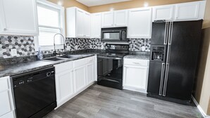 A modern kitchen with white cabinets, a black refrigerator, a microwave, and a dishwasher.