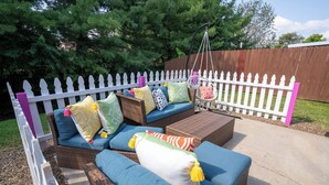 An outdoor seating area with wicker furniture, cushions, and a hanging chair.