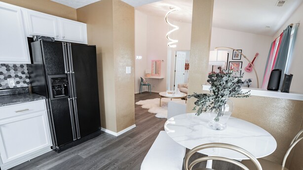 A modern kitchen with a black refrigerator, white cabinets, and a marble dining table with chairs.