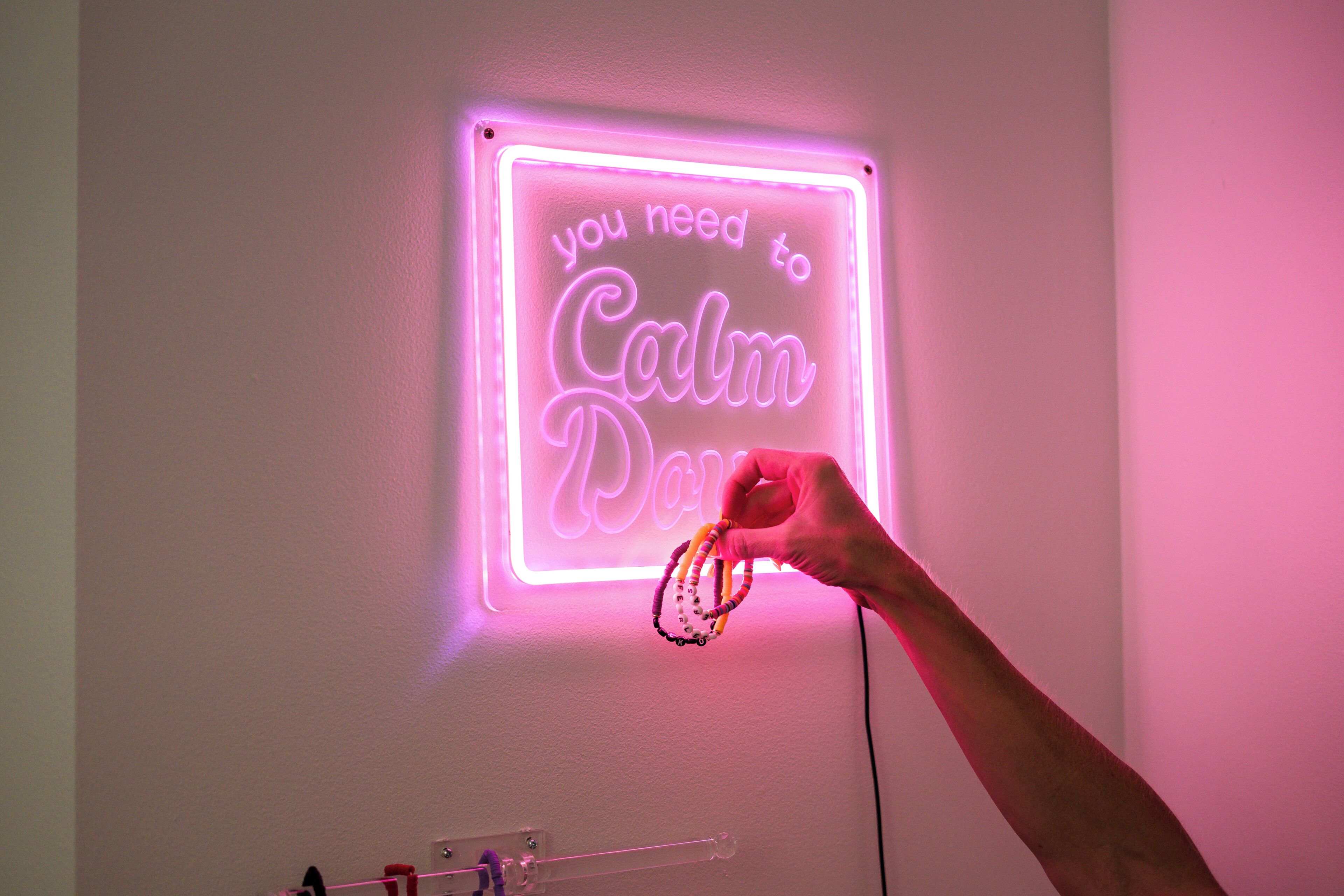 Ein Neonlichtschild mit dem Text 'you need to Calm Down' an einer weißen Wand.