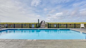 A swimming pool with a wooden deck, a lifeguard stand, and a view of the beach. - Emerald Surf 204 (Navarre)