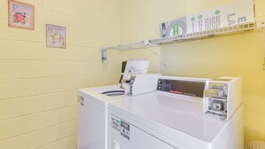 A laundry area with a front-loading washer, a dryer, and a shelf above the dryer with a sign. - Emerald Surf 204 (Navarre)