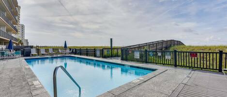 A swimming pool with a wooden deck, a fence, and a building in the background.
