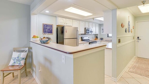 A kitchen with white cabinets, a central island, a refrigerator, a microwave, and a chalkboard with a message. - Emerald Surf 204 (Navarre)