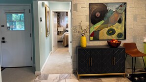 A hallway with a patterned wall, a black cabinet with gold handles, a yellow vase with branches, and a painting. - Fiesta !-Fantastic 1-bedroom apartment with AC in charming Covington (Covington)
