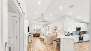 A modern kitchen with white cabinets, a central island, and a dining area with wooden flooring. - 🦩Book Me Baby! Sweet Retreat in Miramar~Golf Cart Included🦩 (Miramar Beach)