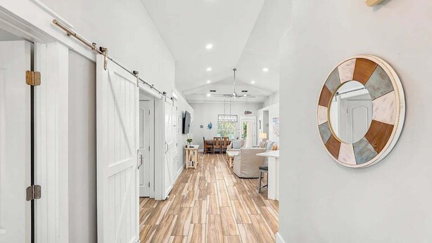 A hallway with white doors, a dining area with a table and chairs, and a round mirror on the wall. - 🦩Book Me Baby! Sweet Retreat in Miramar~Golf Cart Included🦩 (Miramar Beach)