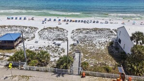 A beach with umbrellas, a white building, and a fenced area. - 🦩Book Me Baby! Sweet Retreat in Miramar~Golf Cart Included🦩 (Miramar Beach)