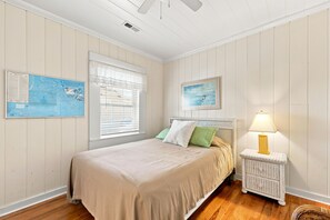 A bedroom with a bed, a nightstand, a lamp, and two wall-mounted maps.