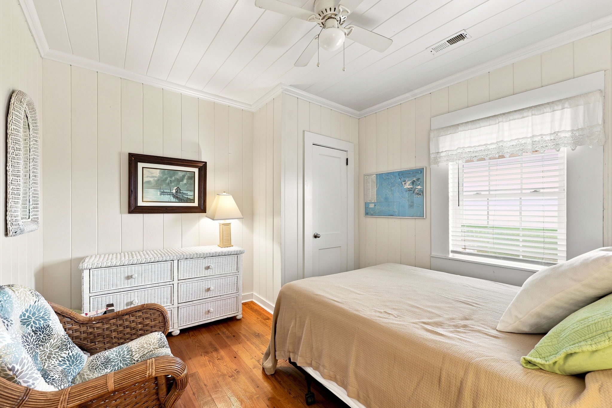 A bedroom with a bed, a dresser, a chair, a lamp, and a map on the wall.